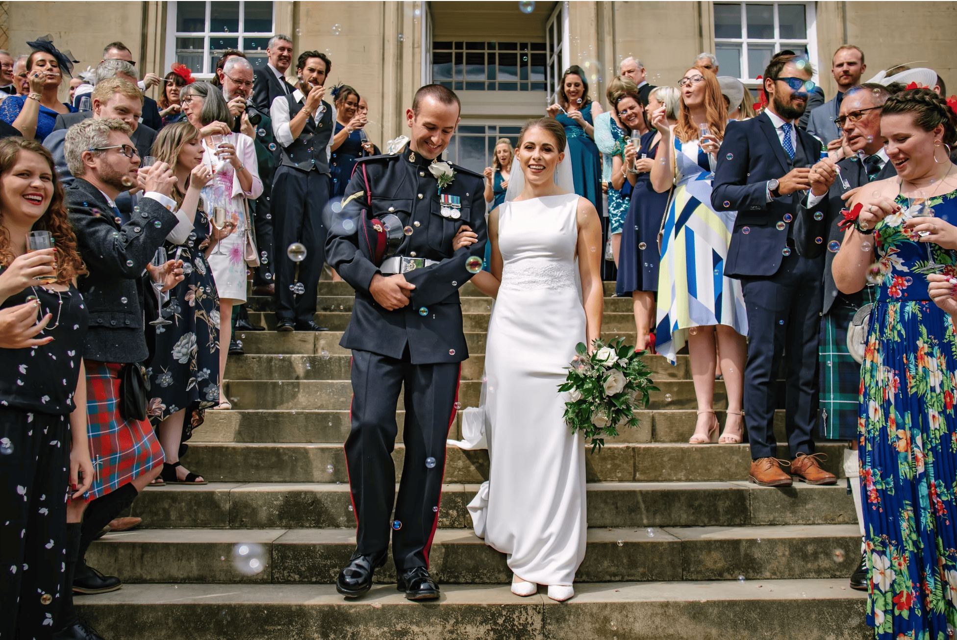 Military bride and groom walk through a bubble send-off surrounded by cheering guests